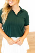 Woman wearing a green polo shirt and white pants on a wooden floor.